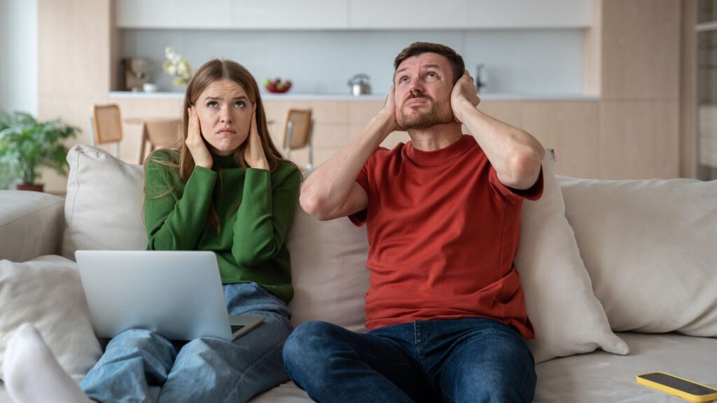 Une femme et un homme qui se bouchent les oreilles à cause d'une mauvaise isolation phonique venant du plafond